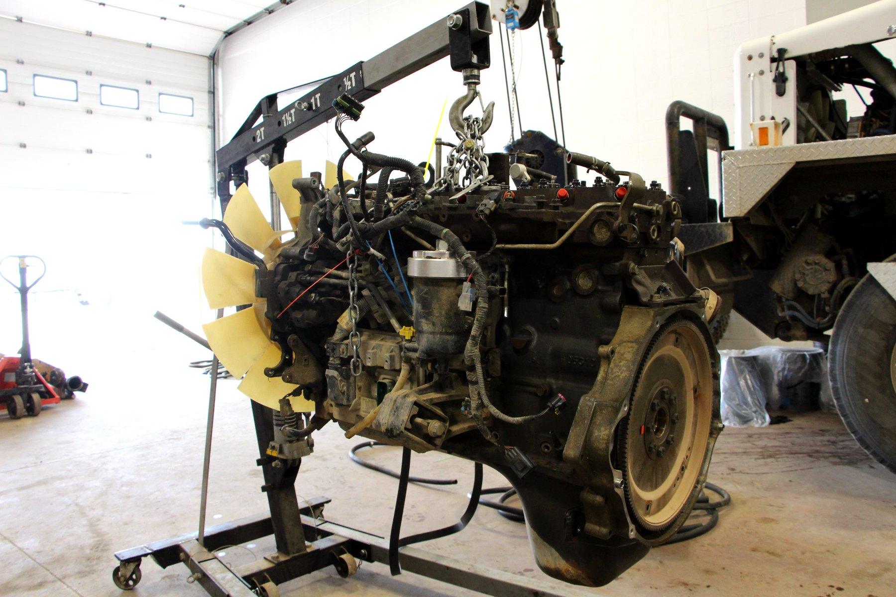 A diesel engine hanging from a shop hoist beside a heavy truck.