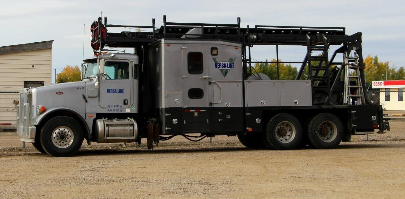 A heavy service truck with a ladder rack and equipment deck parked at a work site.