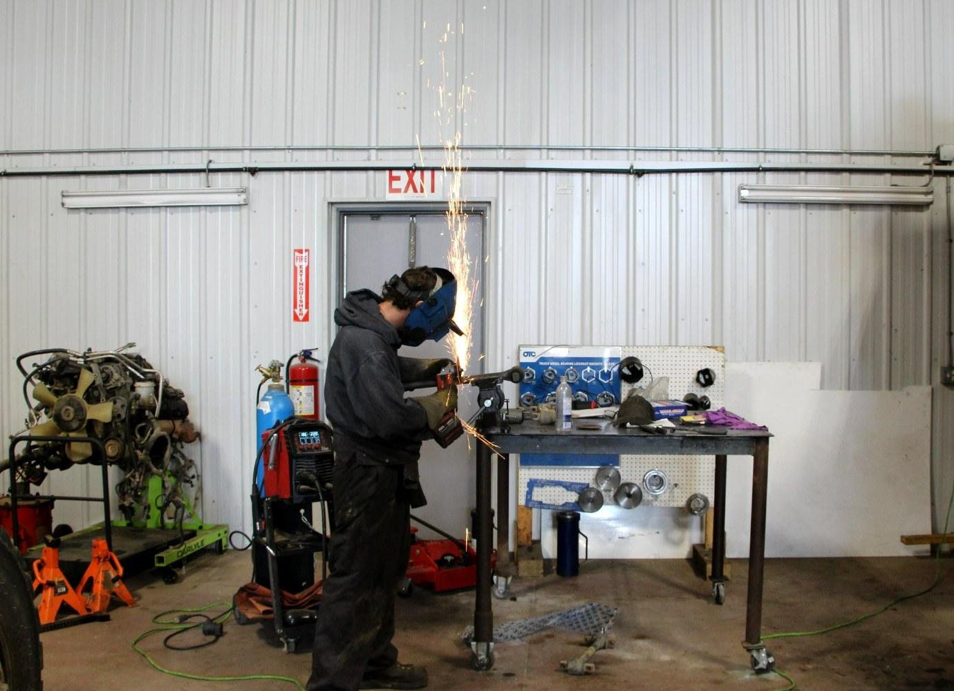 A Big Horn technician in a welding helmet grinding at the shop bench, sparks flying.